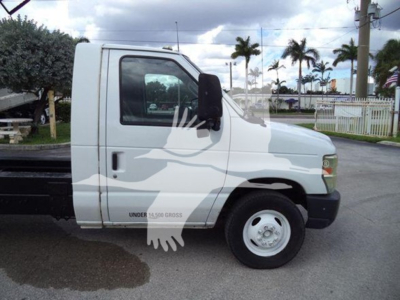 Ford E-450 cab with dump bed side view showing front wheel and door; VIN 1FDXE4FS7BDA10516 stock T10516; utilities and palm trees in background.