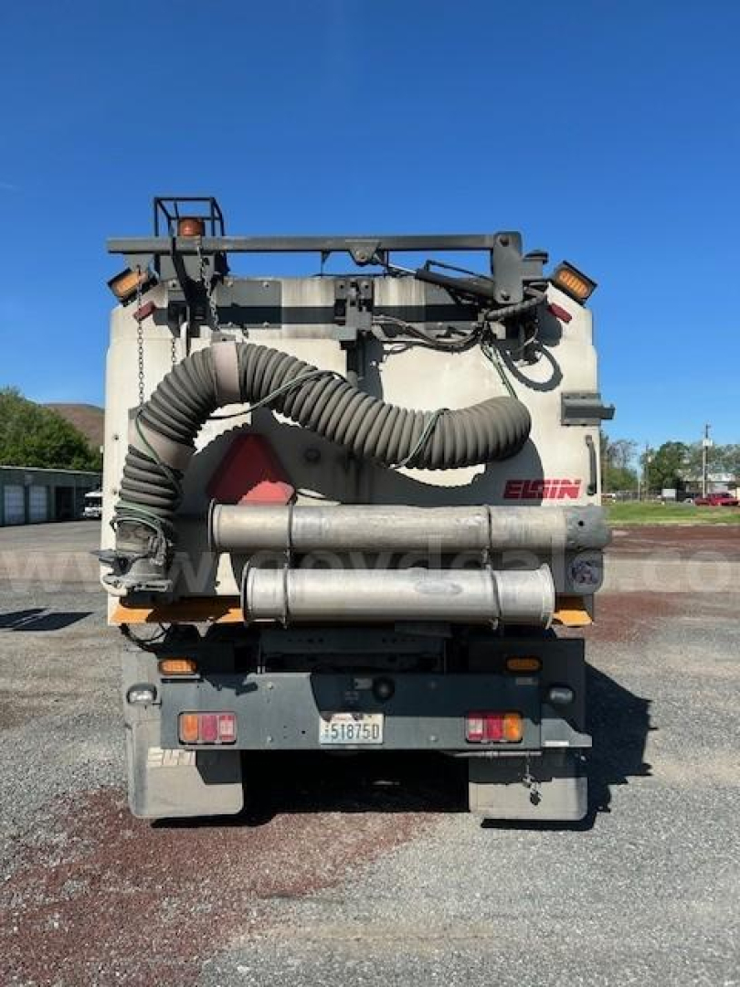 Back of a Freightliner M2 106 sweeper showing large vacuum hose and rear attachments.