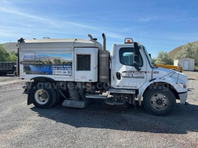 Truck side view of a 2012 Freightliner M2 106 sweeper showing cab and cargo body with trailer hitch and wheel details.