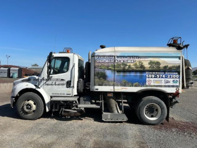 Freightliner M2 106 sweeper truck side view showing advertising graphics on rear tank and front cab with logo text.