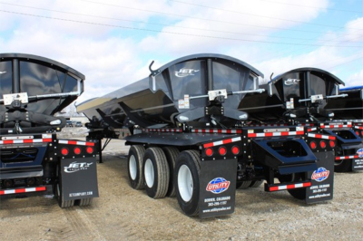 Jet Super Spread side dump trailer showing multiple dump bodies on a lowboy with dual rear axles and tire stacks, branding and reflective safety tape visible.
