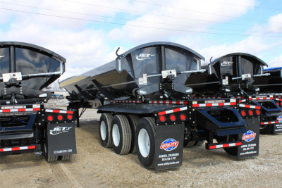 Jet super spread side dump trailers trailer bed with black bodies and triple axles, showing IET branding and utility trailers signage on mud flaps and rear ramps.