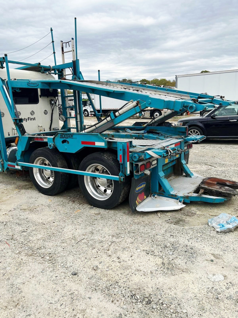 Peterbilt 389 auto carrier truck trailer in blue with hydraulic ramps and dual rear axles, side view showing loading equipment and tires.