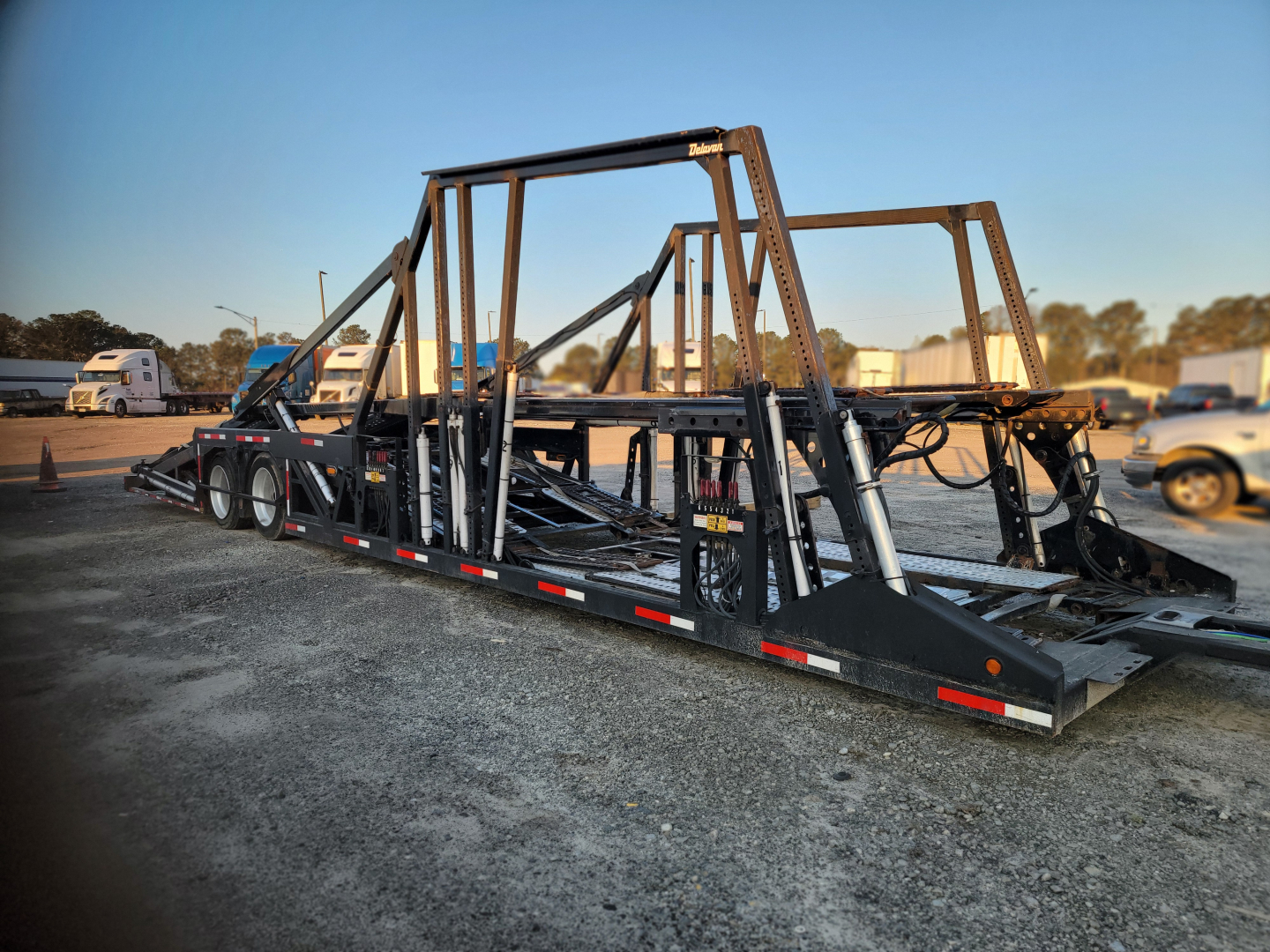 Peterbilt 389 car carrier trailer with metal framework and ramps, side railings and hydraulic components in an open lot.