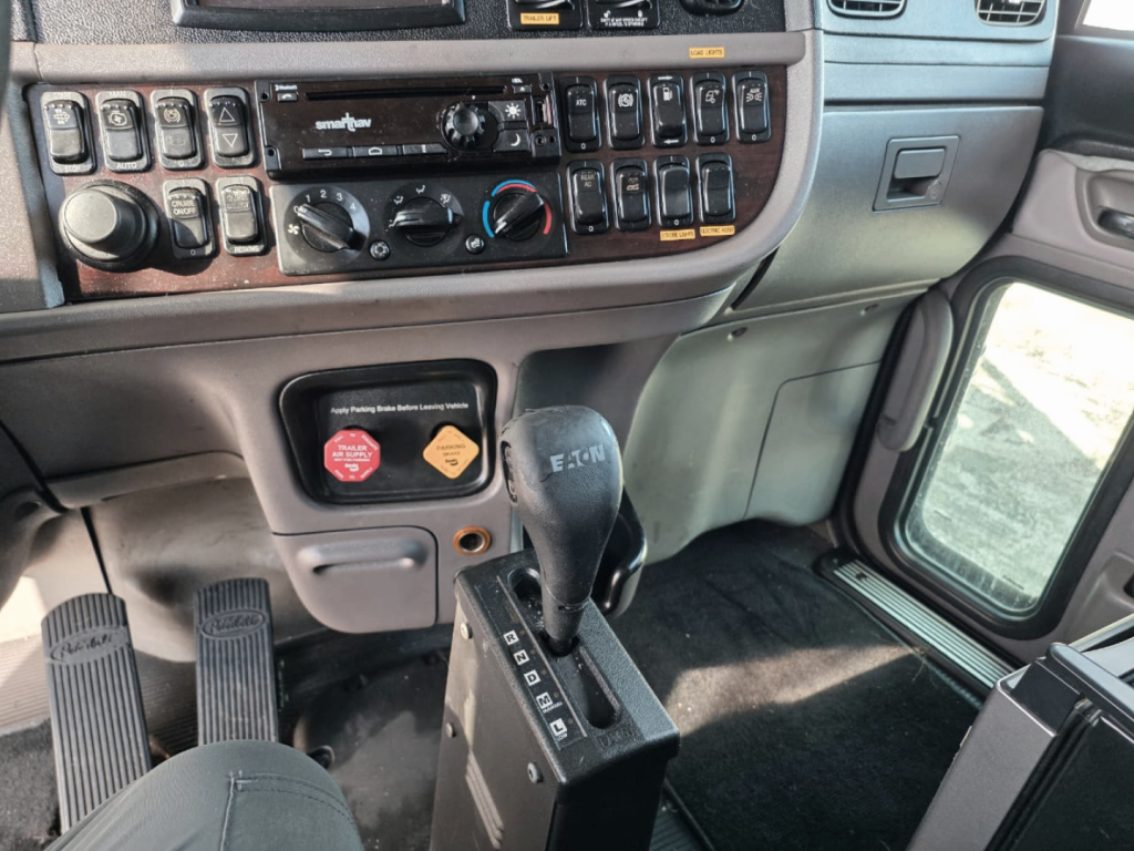 Interior view of a 2019 Peterbilt 389 truck cab showing gear shifter and dashboard with multiple control switches and climate controls.