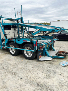 Peterbilt 389 auto carrier truck trailer in blue with hydraulic ramps and dual rear axles, side view showing loading equipment and tires.