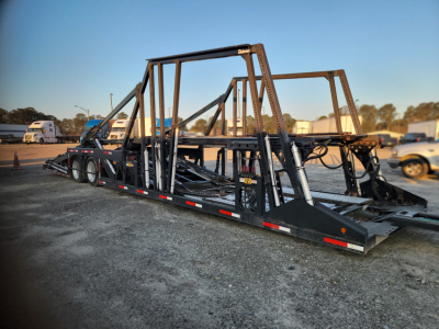 Peterbilt 389 car carrier trailer with metal framework and ramps, side railings and hydraulic components in an open lot.