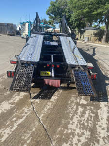 Truck trailer loading deck for a 2019 Peterbilt 389 in carrier configuration, with perforated metal ramps extended, rear view, and license plate visible.