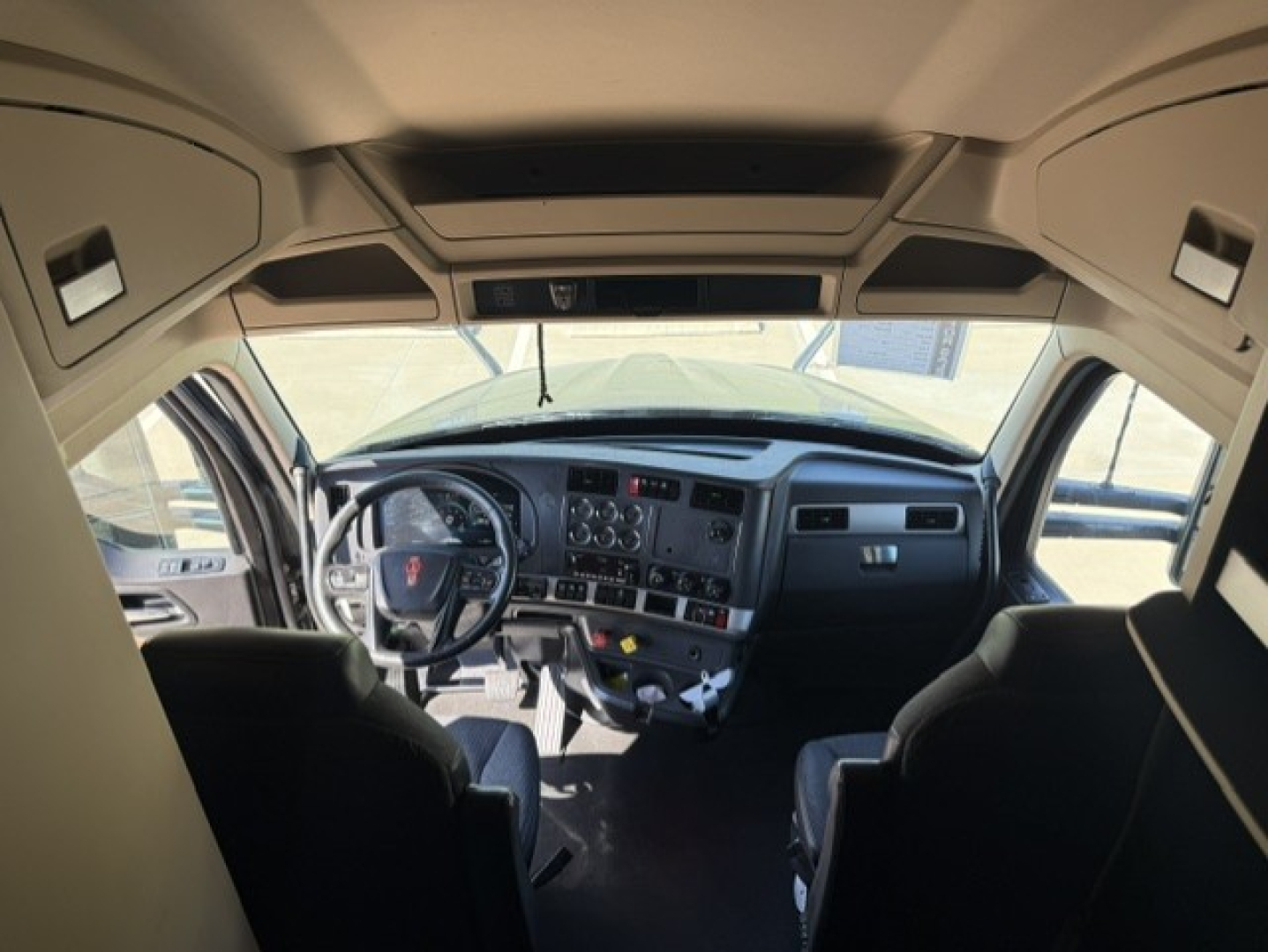 Truck cab interior view of a 2023 Kenworth T680 with steering wheel, dashboard, and front seats visible.