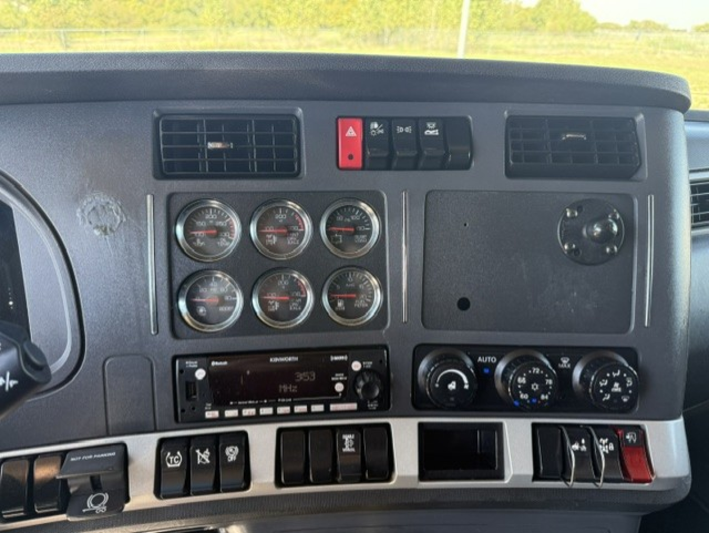 Kenworth T680 dash panel showing multiple gauges, climate controls, switches, and a stereo head unit.
