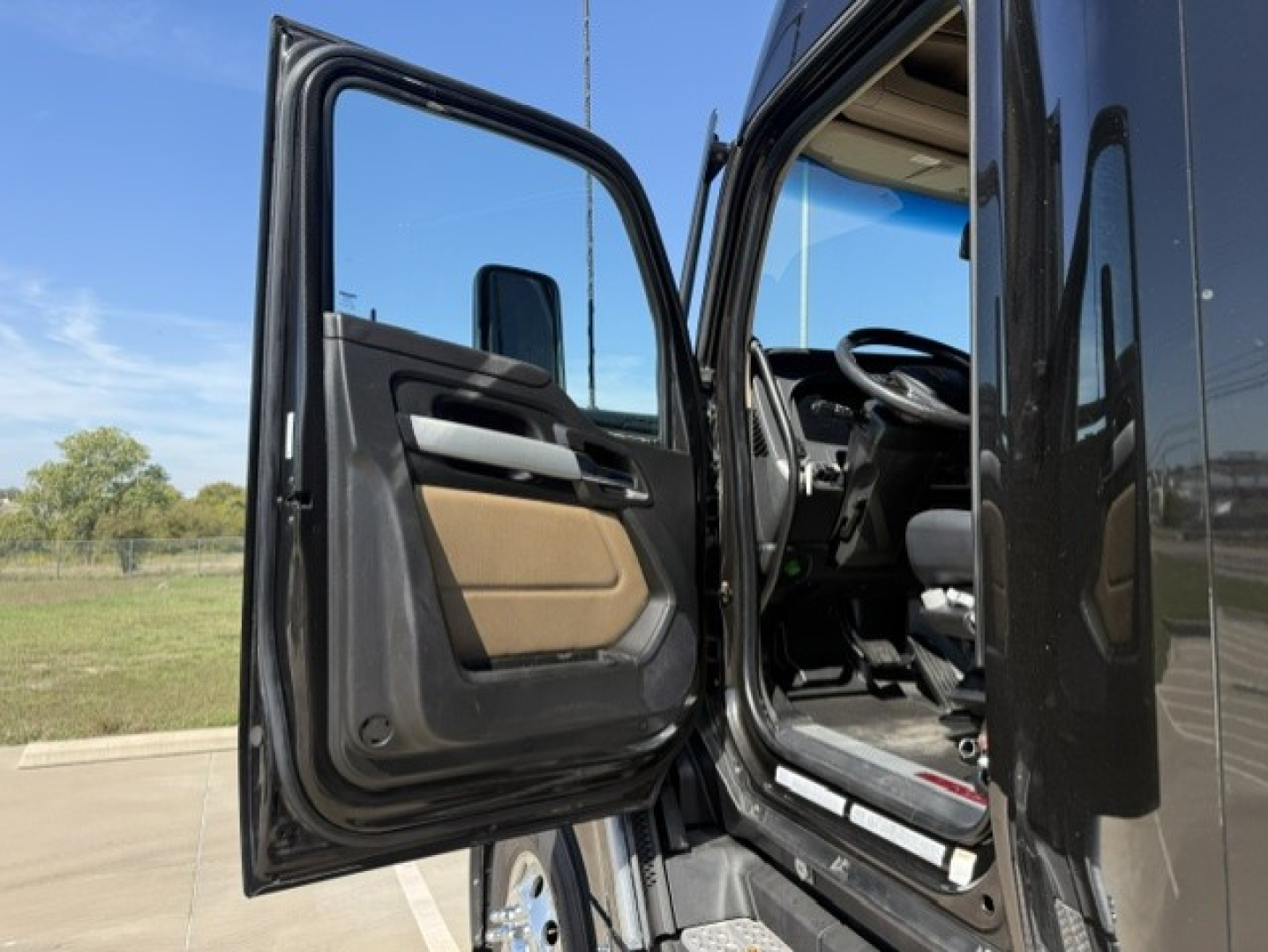Kenworth T680 cab doorway and interior view from open driver door showing steering wheel and driver's seat.