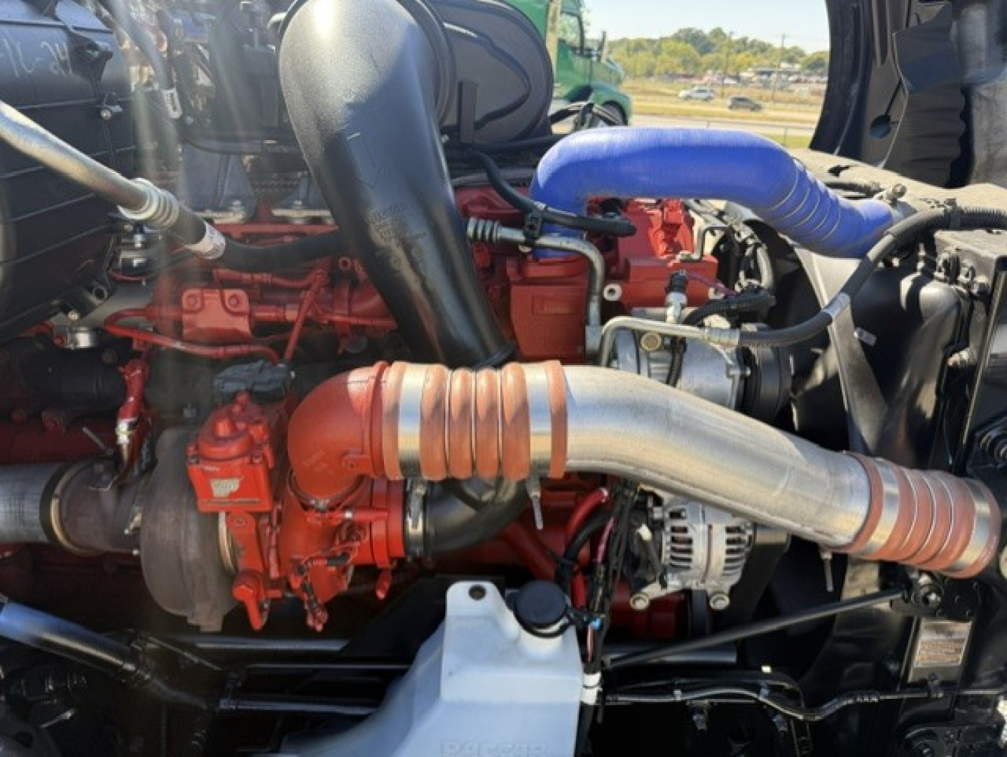 Kenworth T680 engine bay showing red turbocharger and silver exhaust pipe with blue silicone hose and black intake piping.