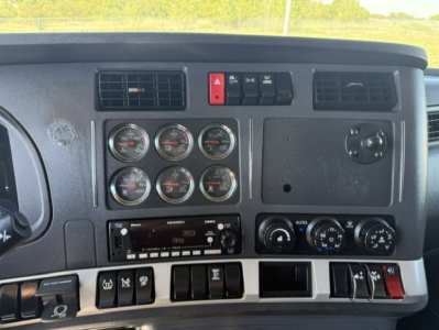 Kenworth T680 dash panel showing multiple gauges, climate controls, switches, and a stereo head unit.