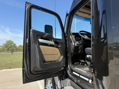 Kenworth T680 cab doorway and interior view from open driver door showing steering wheel and driver's seat.