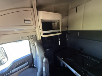 Cab interior of a 2023 Kenworth T680 sleeper truck showing overhead storage cabinet with open microwave shelf and cockpit area.