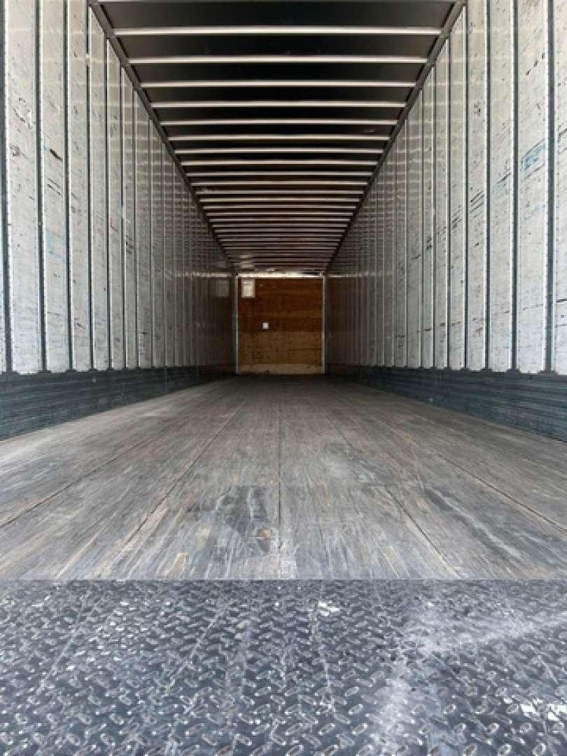 Trailer interior showing empty cargo area with wooden bulkhead at back, metal side walls, and textured floor