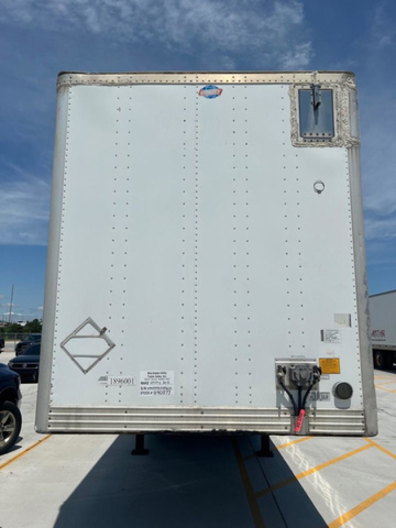 Rear view of a white utility van trailer showing back doors, riveted panels, and a rear bumper with electrical/air connections and reflective stickers.
