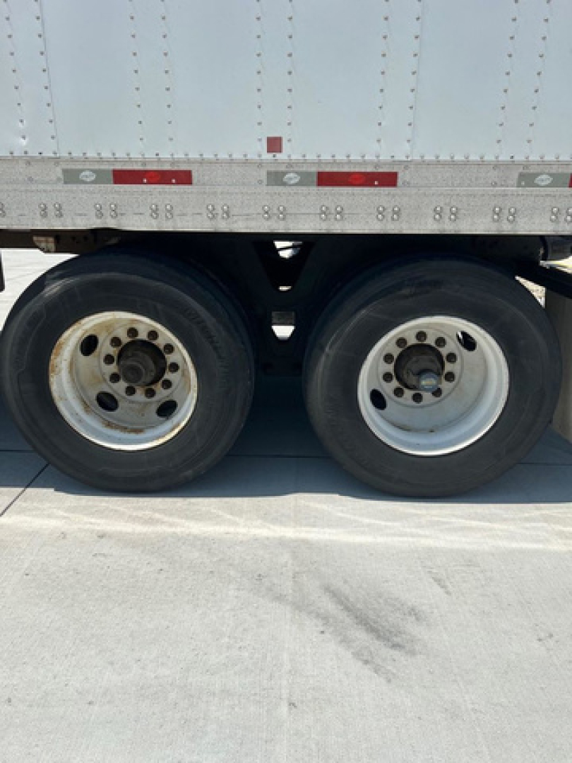 Dual trailer wheels and undercarriage of a utility van trailer showing wheel rims and tires.
