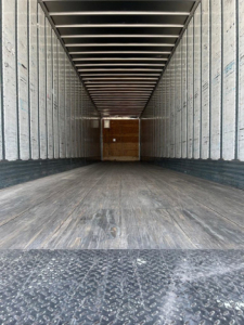 Trailer interior showing empty cargo area with wooden bulkhead at back, metal side walls, and textured floor