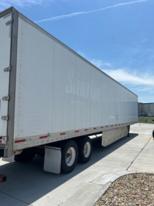 Trailer side view showing a white semi-trailer with faded lettering and tandem axle wheels.
