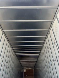 Trailer interior showing metal wall panels and ribbed ceiling with linear crossbars, long tunnel-like cargo area