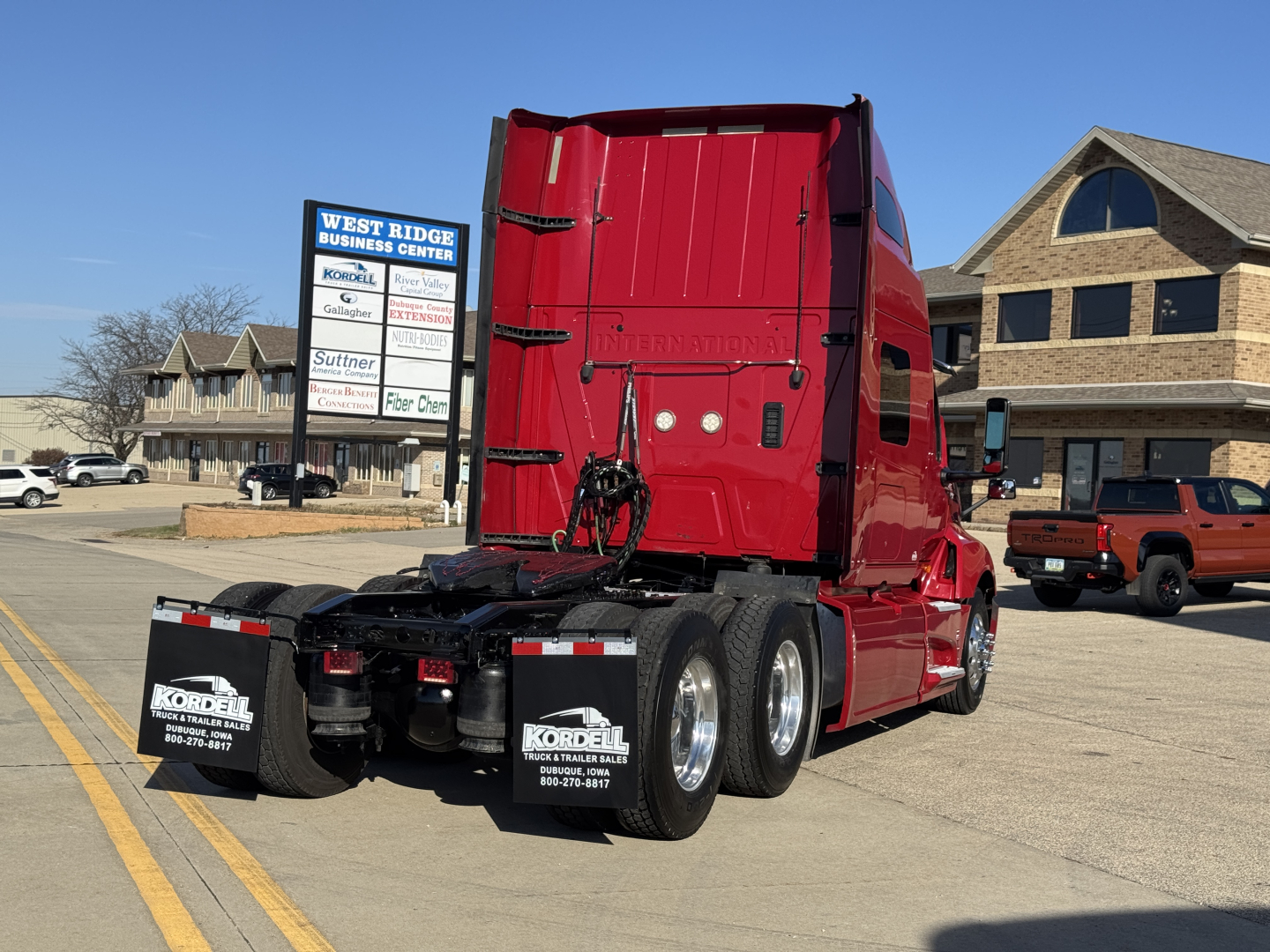 Truck tractor rear view showing red International LT625 with triple rear axles and black mud flaps; visible text on mud flaps and rear, VIN and stock info not on vehicle.