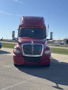 Truck front view of a burgundy 2018 International LT625 sleeper tractor, with large chrome grille, prominent hood, tall aerodynamic roof fairing, and side mirrors.