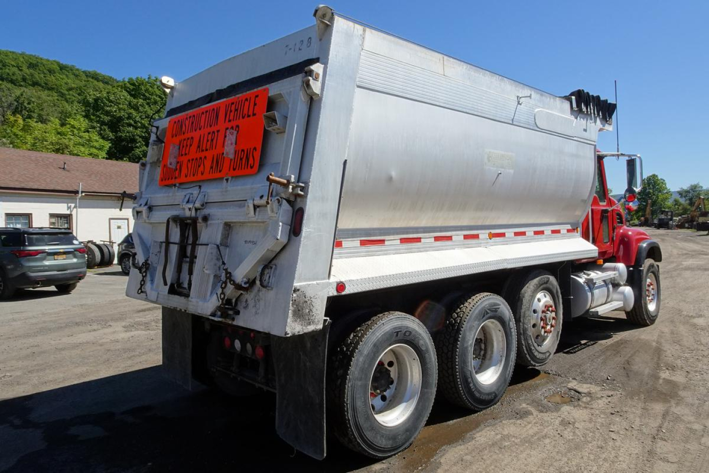 Dump truck rear and side view showing Mack CV Granite dump body with safety sign and stacked dual rear wheels.