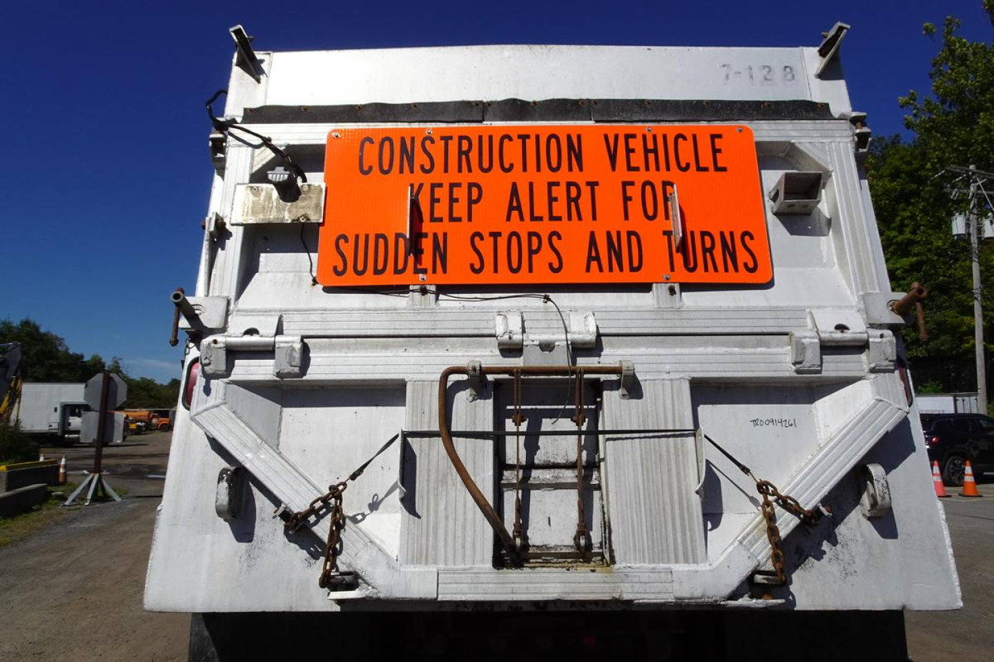 Back of a white construction dump truck with an orange warning sign reading "CONSTRUCTION VEHICLE KEEP ALERT FOR SUDDEN STOPS AND TURNS"