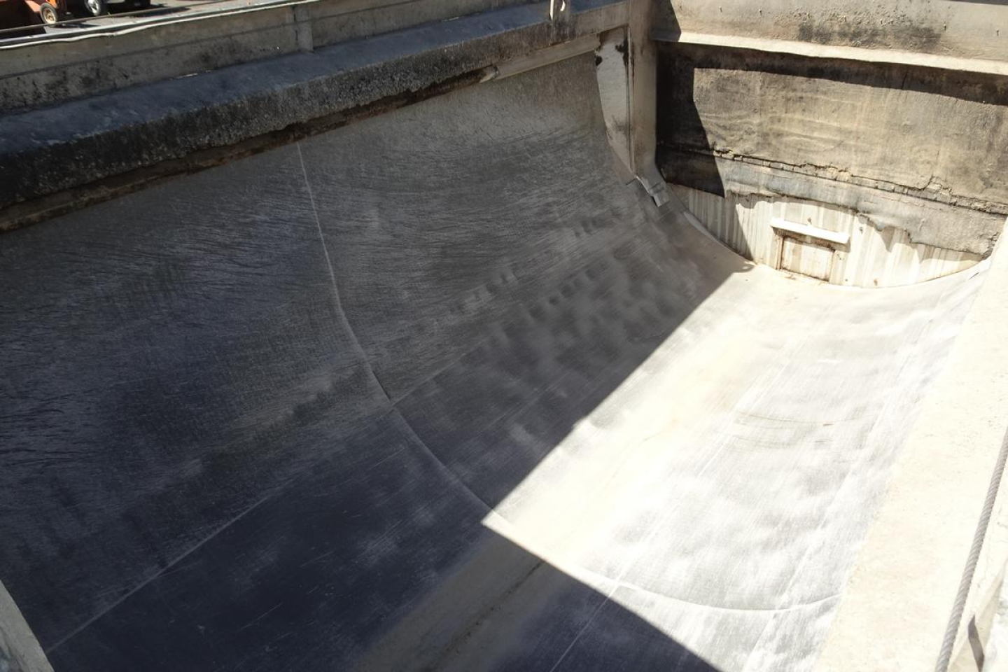 Inside of dump truck bed showing smooth metal surface with worn edges and channels. No identifiable text visible.