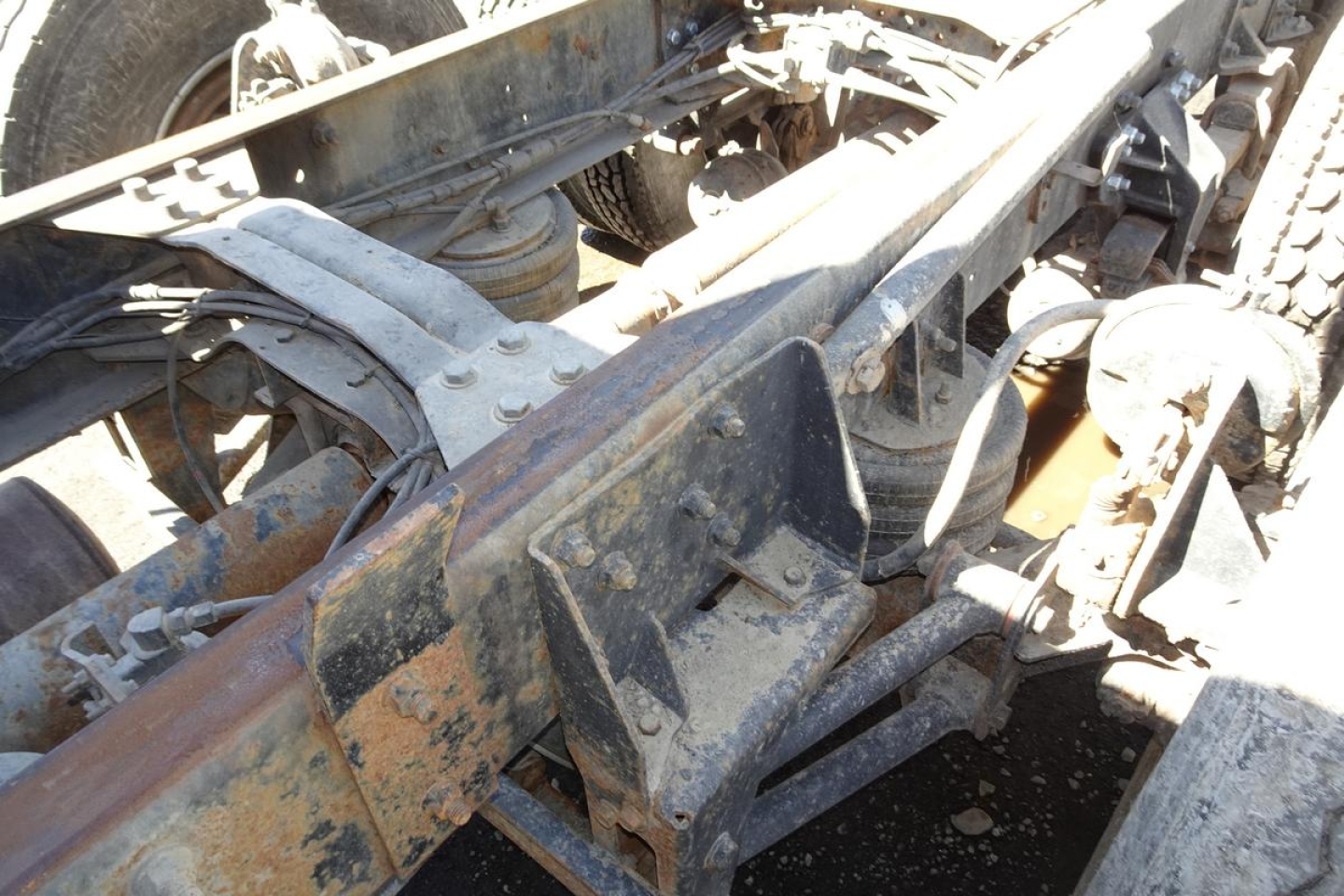 Dump truck chassis components with metal brackets and hydraulic lines visible, showing a scratched, rust-toned frame and mounting hardware.