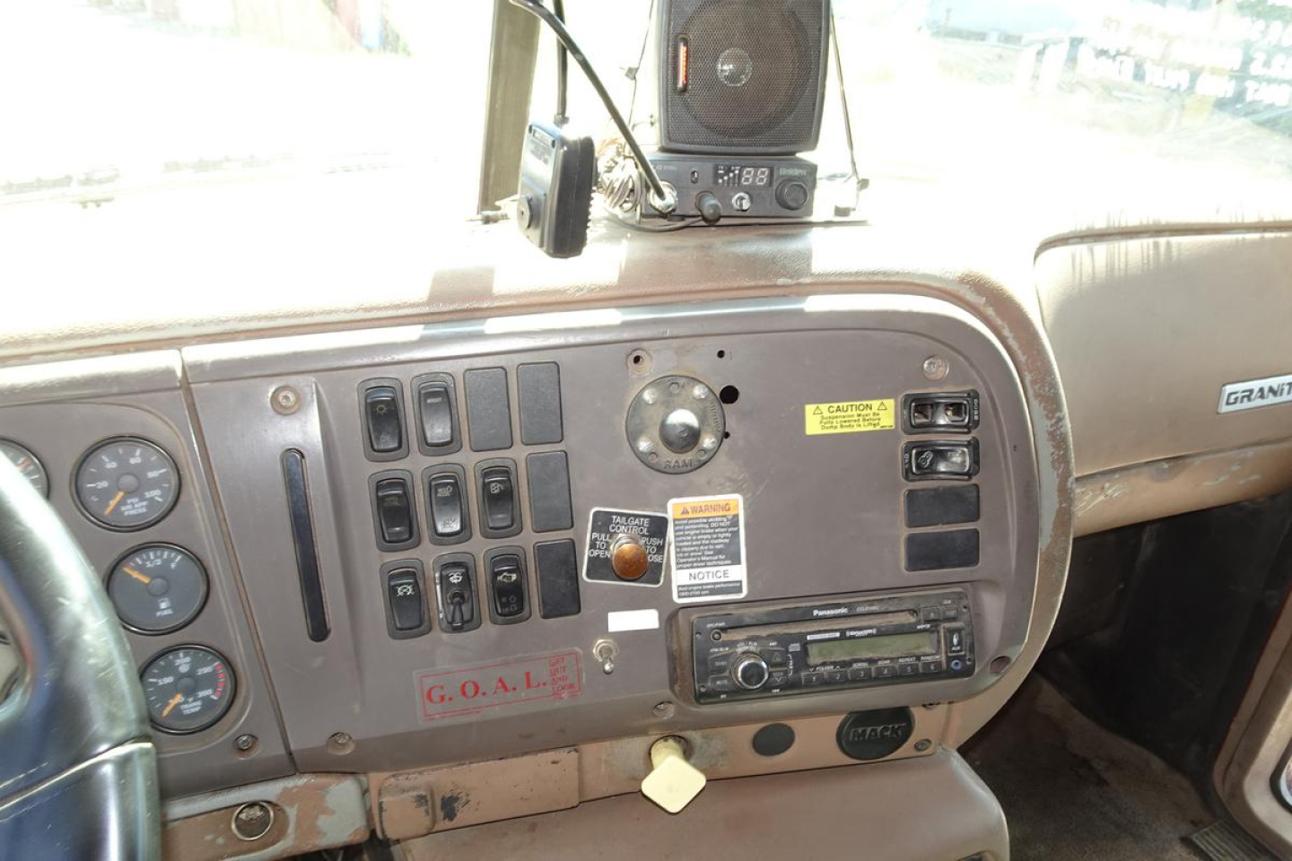 Truck dashboard of a Mack CV (Granite) CV713 showing gauge cluster, control switches, and radio panel with decals and stickers.