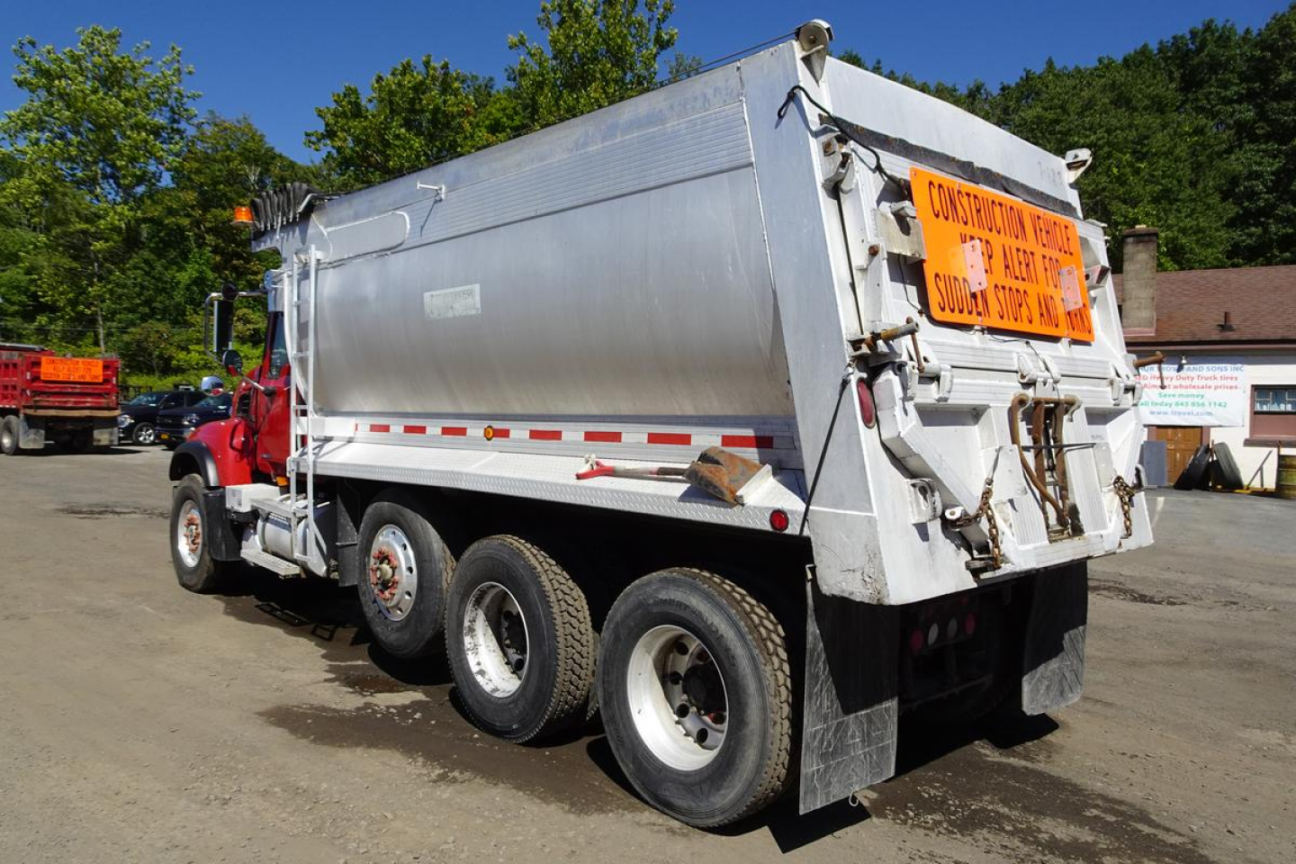 Dump truck rear and side view showing Mack CV Granite CV713 with silver dump body and orange warning sign on tailgate.