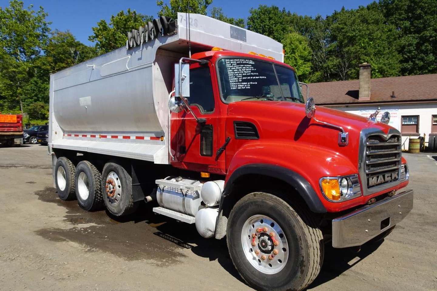 Mack CV Granite dump truck side view showing red cab and silver dump bed with multiple axles.