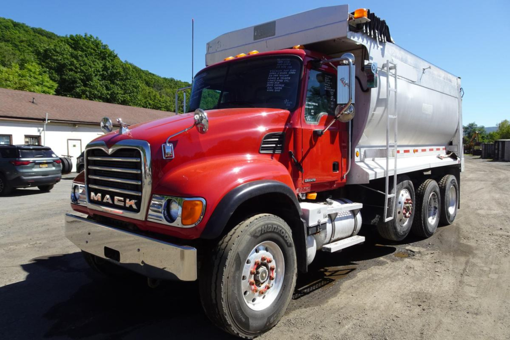 Mack CV granite dump truck in red and white, front three-quarter view showing chrome grille, large front bumper, dual rear axles, and dump body.