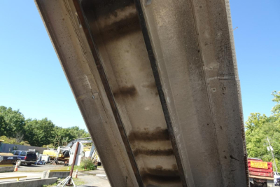 Concrete dump truck bed underside with riveted steel side walls and support beams.