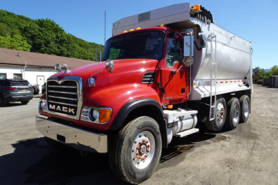 Mack CV granite dump truck in red and white, front three-quarter view showing chrome grille, large front bumper, dual rear axles, and dump body.