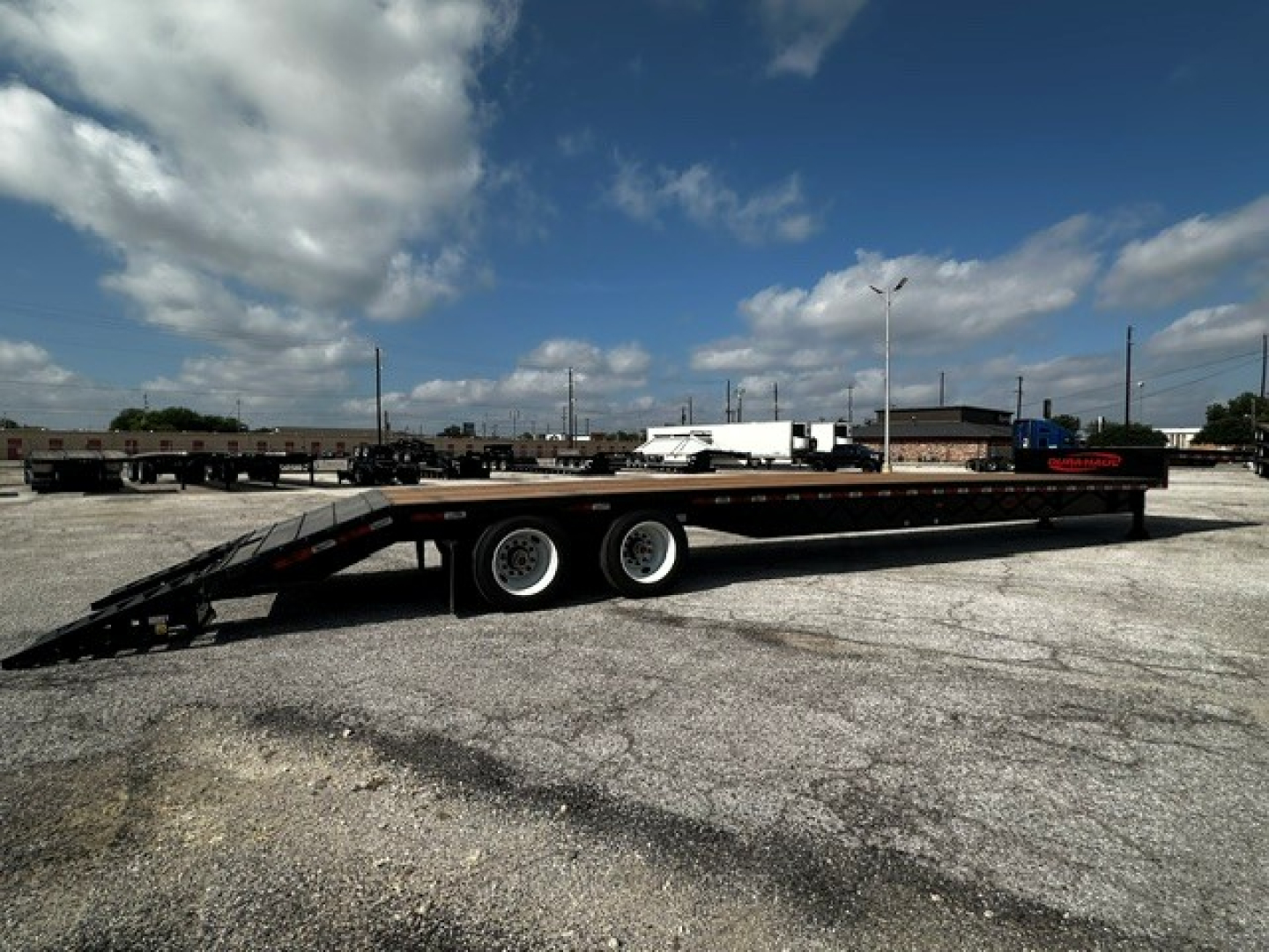 Trailer side view: 53' drop deck with closed tandem wheels and foldable ramps at rear; black flatbed with tandem axle configuration.