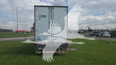 Rear view of a white 2019 Stoughton plate van trailer with 'SPRINT' branding on the upper left door; two vertical doors, DOT reflective tape along lower edge, grass field and other trucks in background.