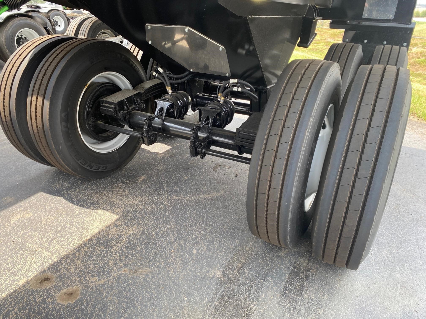 Frameless steel rock end dump trailer undercarriage showing dual rear axles with leaf springs and dual tires, black chassis, and suspension components.