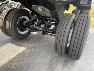 Trailer undercarriage showing dual rear axles with leaf-spring suspension and dual tires; chassis and suspension components visible.