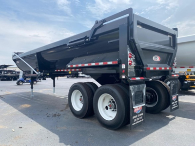 Frameless steel rock end dump trailer showing dual rear axles and black body with reflective stripe and hydraulic tailgate.