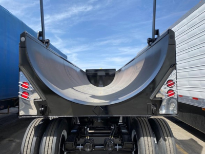 Trailer tail showing frameless steel rock end dump bed with curved underside and dual rear wheels on a dump trailer.