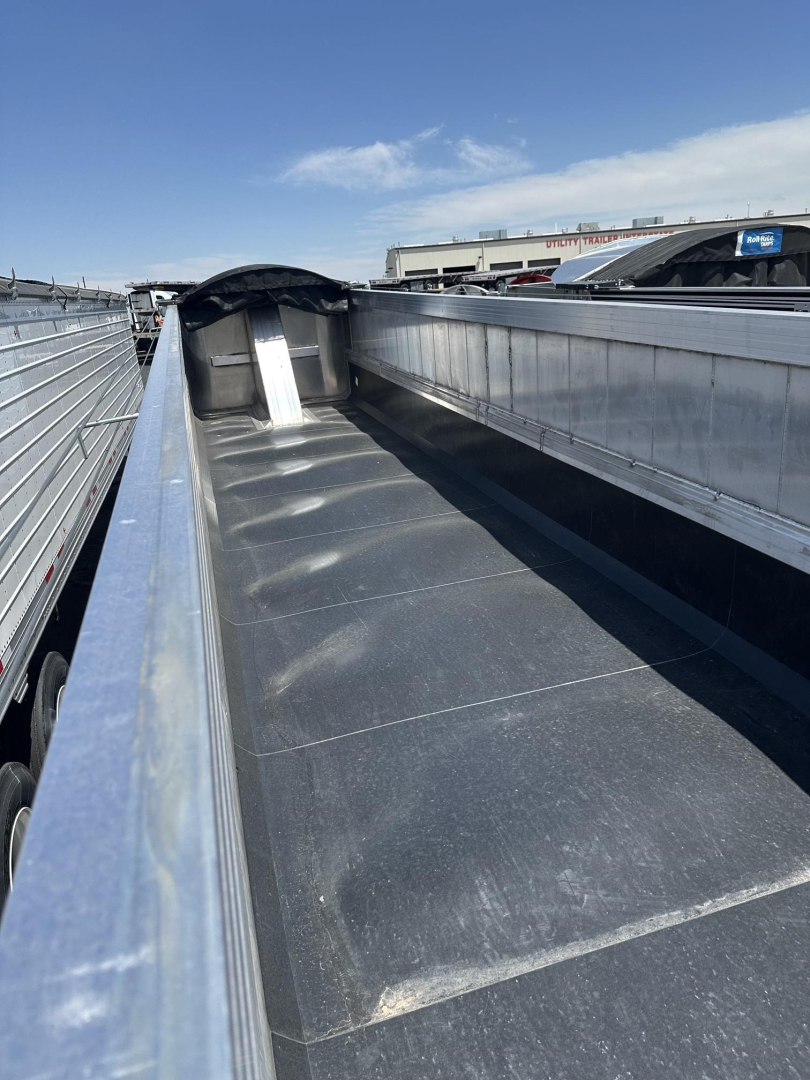 Trailer interior showing frameless aluminum end dump bed with side walls and front bulkhead, flat black surface, reflective metal edges, open top.