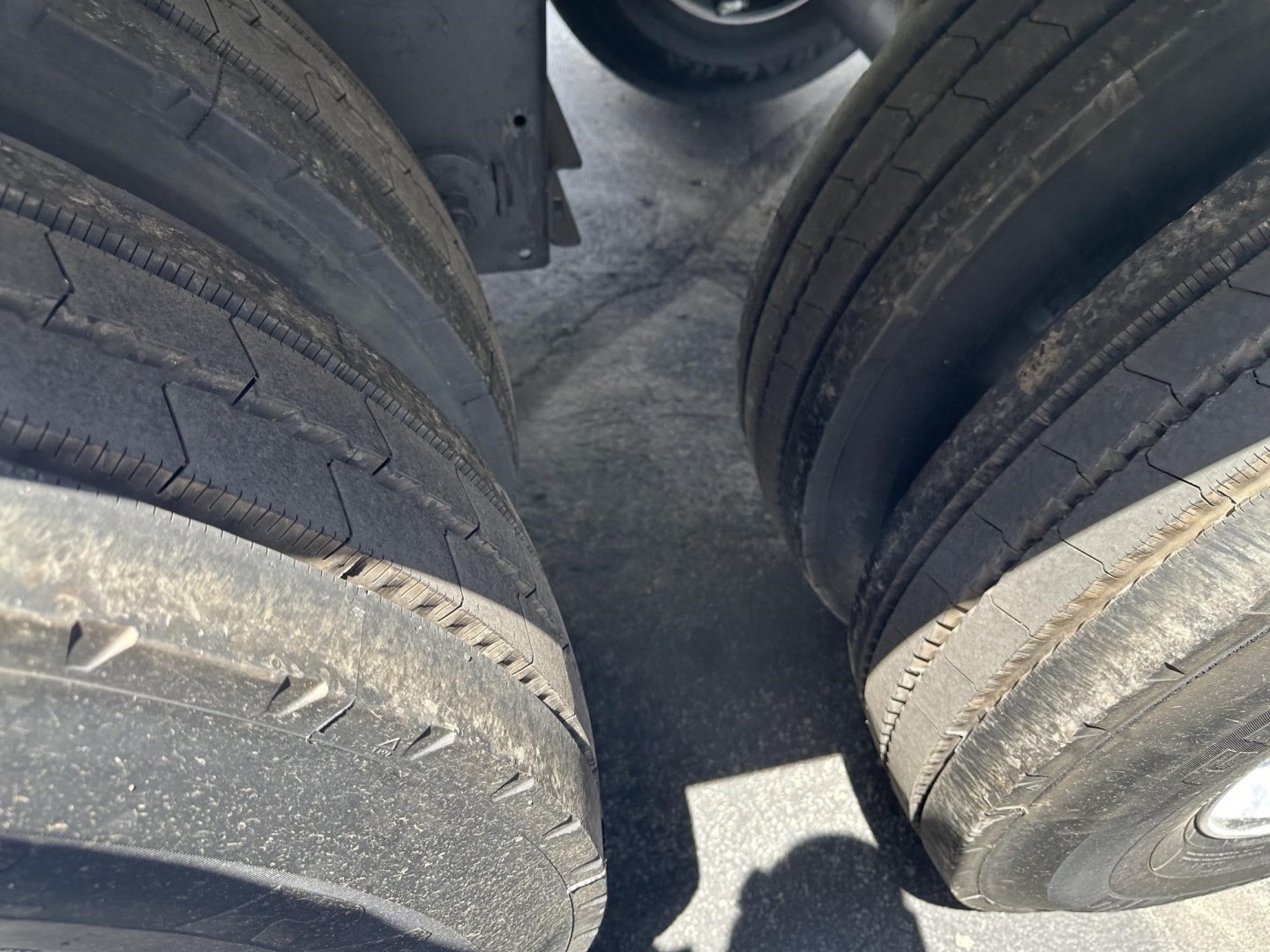 Trailer dual axle tire tread view with dark frame undercarriage; part shows frames and wheel wells.