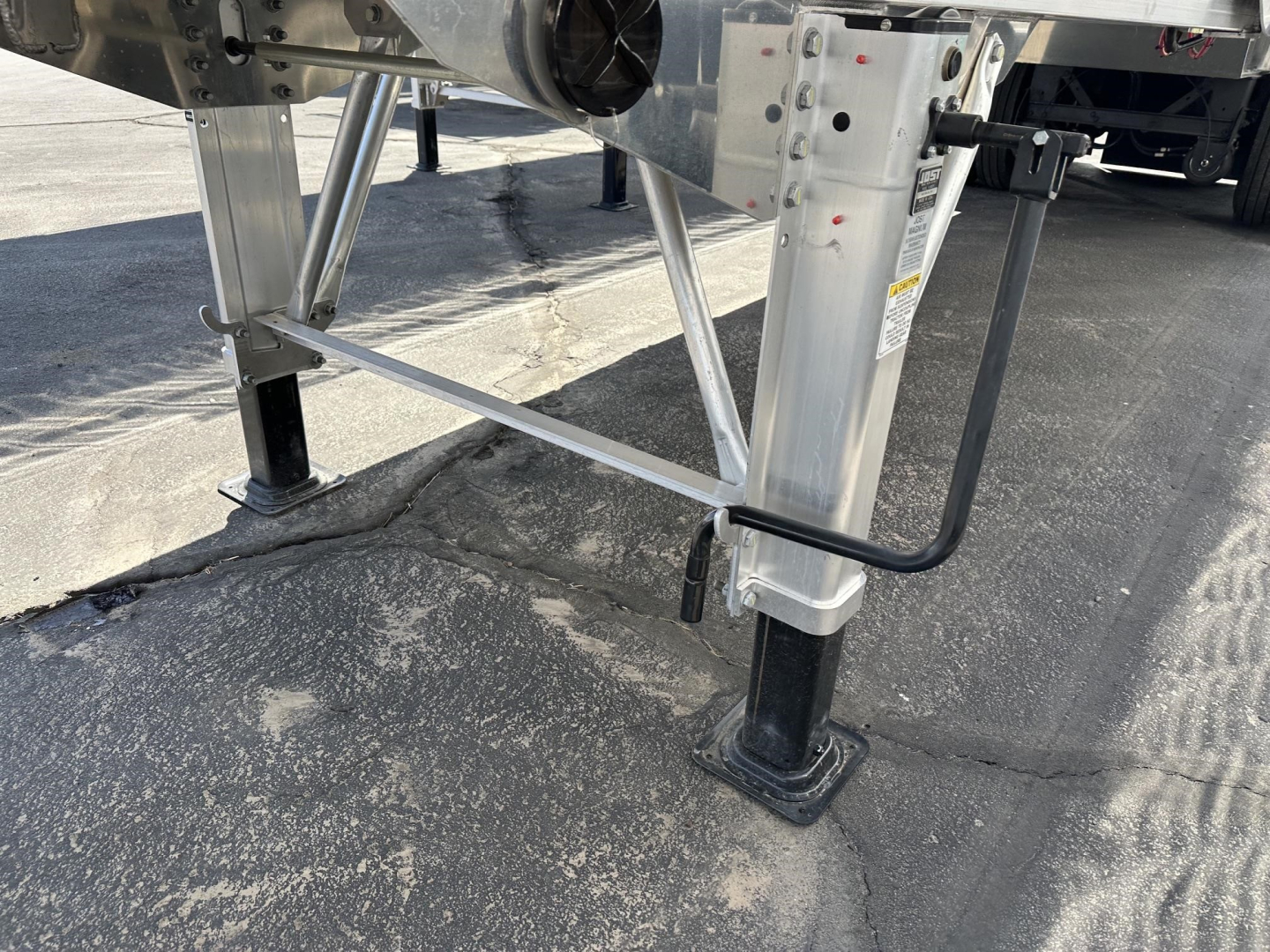 Trailer landing gear and frame of a 2027 Mac lightweight frameless aluminum end dump showing adjustable legs and hydraulic support with visible VIN plate area