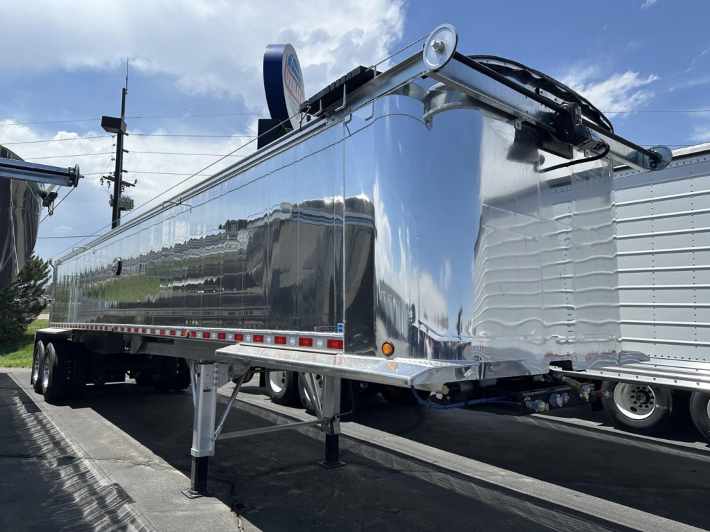 Trailer side view showing a polished aluminum end dump trailer with frameless design and tandem axles.