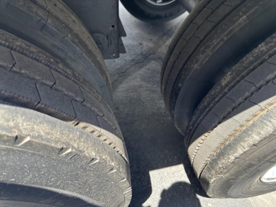 Trailer dual axle tire tread view with dark frame undercarriage; part shows frames and wheel wells.