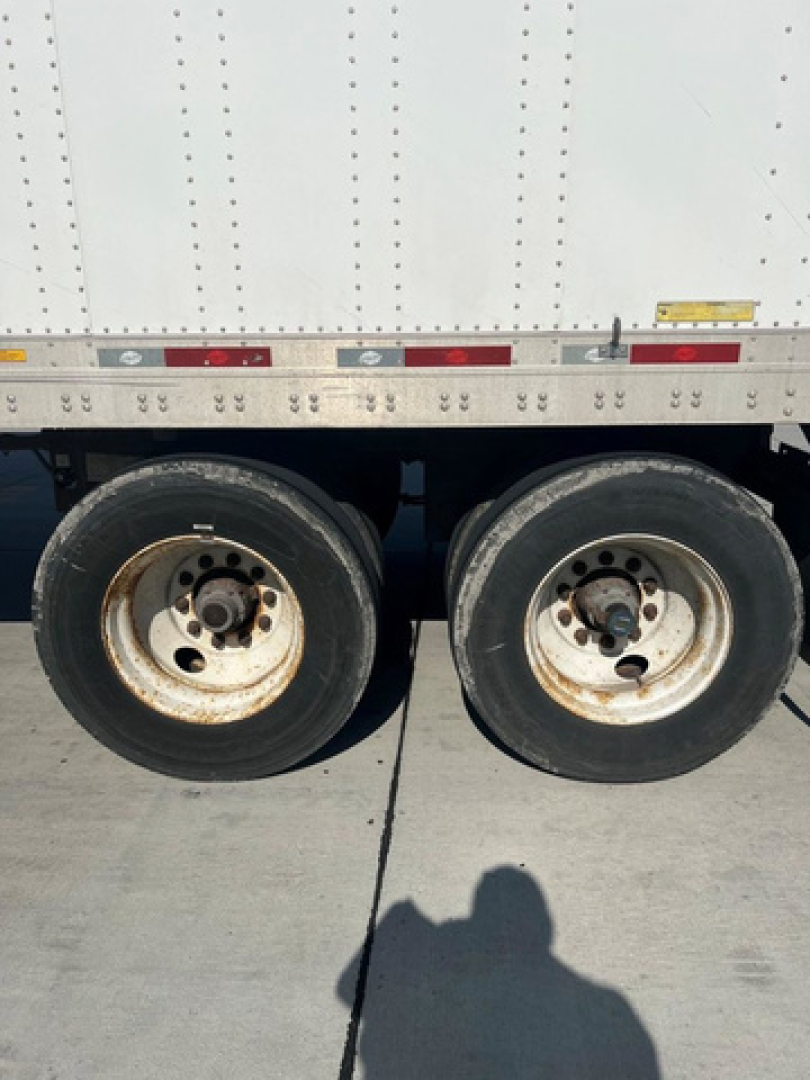 Dual rear trucks on a used 2014 utility van trailer showing two wheels and part of the aluminum ribbed side with reflective tape.