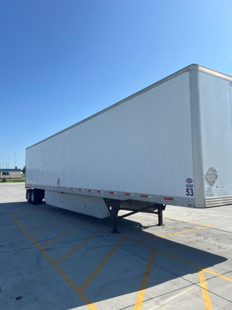 Box trailer from side view showing raised landing gear and white exterior with DOT placards and sticker numbers.